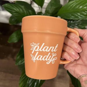 A hand holding terracota pot shaped coffee mug