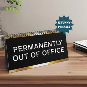 A black and gold desk flipbook with the text Permanently Out of Office printed in large white letters on the front panel, displayed on a warm wooden desk surface