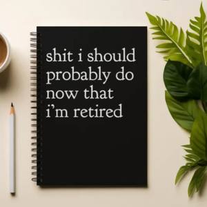 A black spiral bound notebook with white text displayed flat on a cream surface next to a white coffee cup and a green tropical leaf.