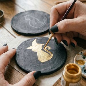 Hand painting a gold cat silhouette onto a round black coaster