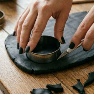 Hands cutting a round coaster shape from a black clay slab
