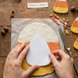 hands holding a candy corn shaped paper stencil over the clay
